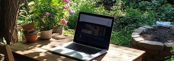 Ordinateur portable ouvert sur une table de bois, dans un jardin planté